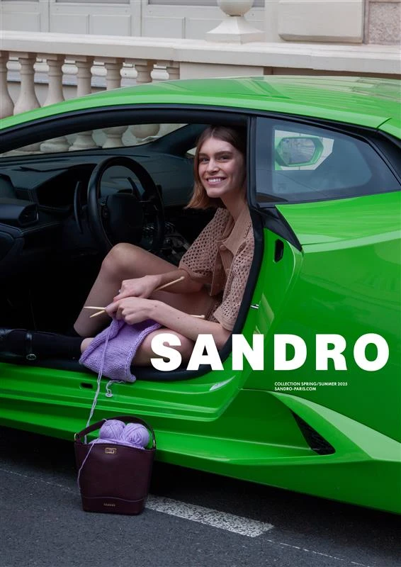 Model sitting in a bright green sports car knitting with purple yarn for Sandro Spring 2025 campaign