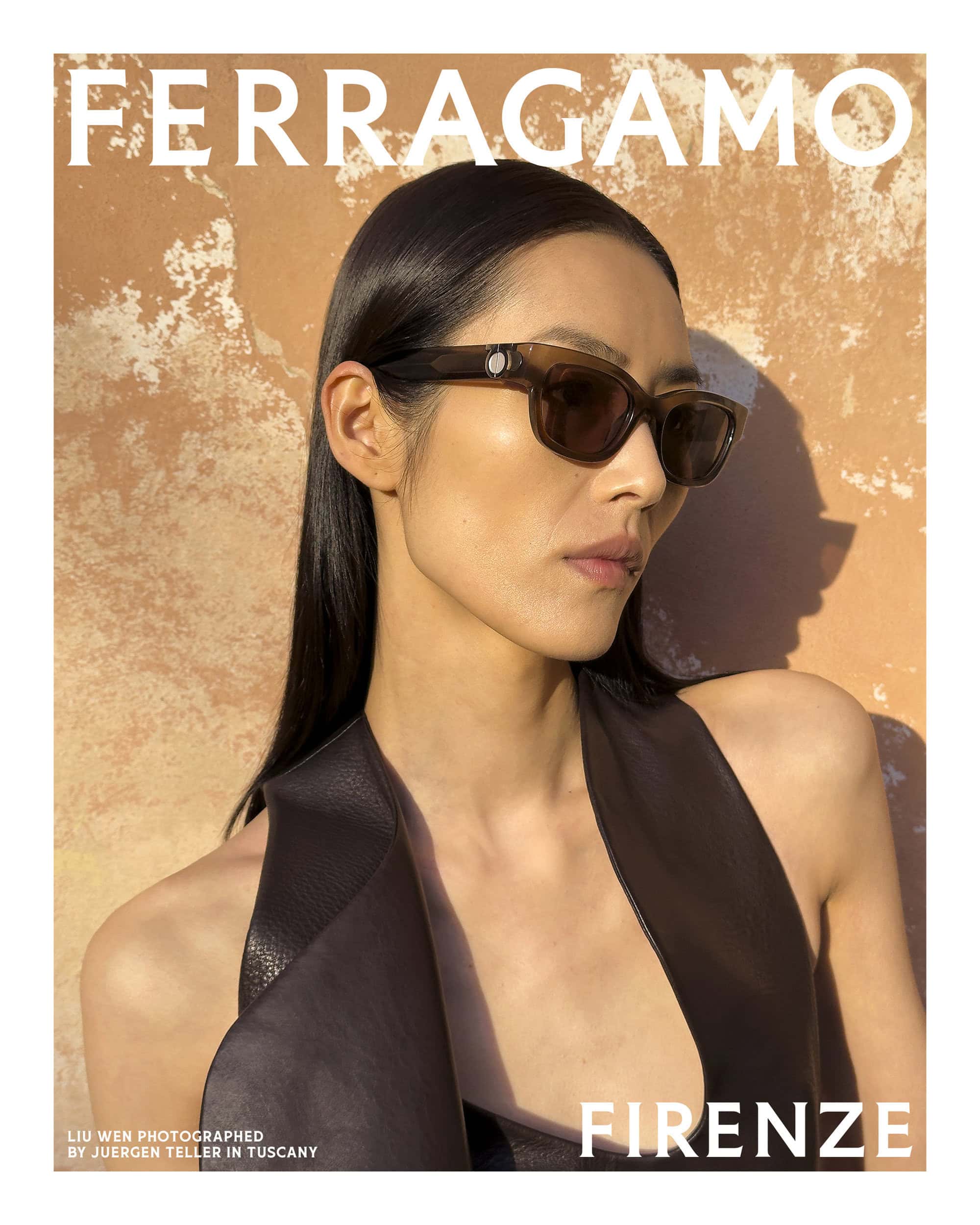 Model wearing dark translucent sunglasses and dark top against a textured stone wall