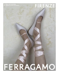 Close-up of legs wearing pale pointed flats with crisscrossed satin pink ribbon ties against a mottled wall