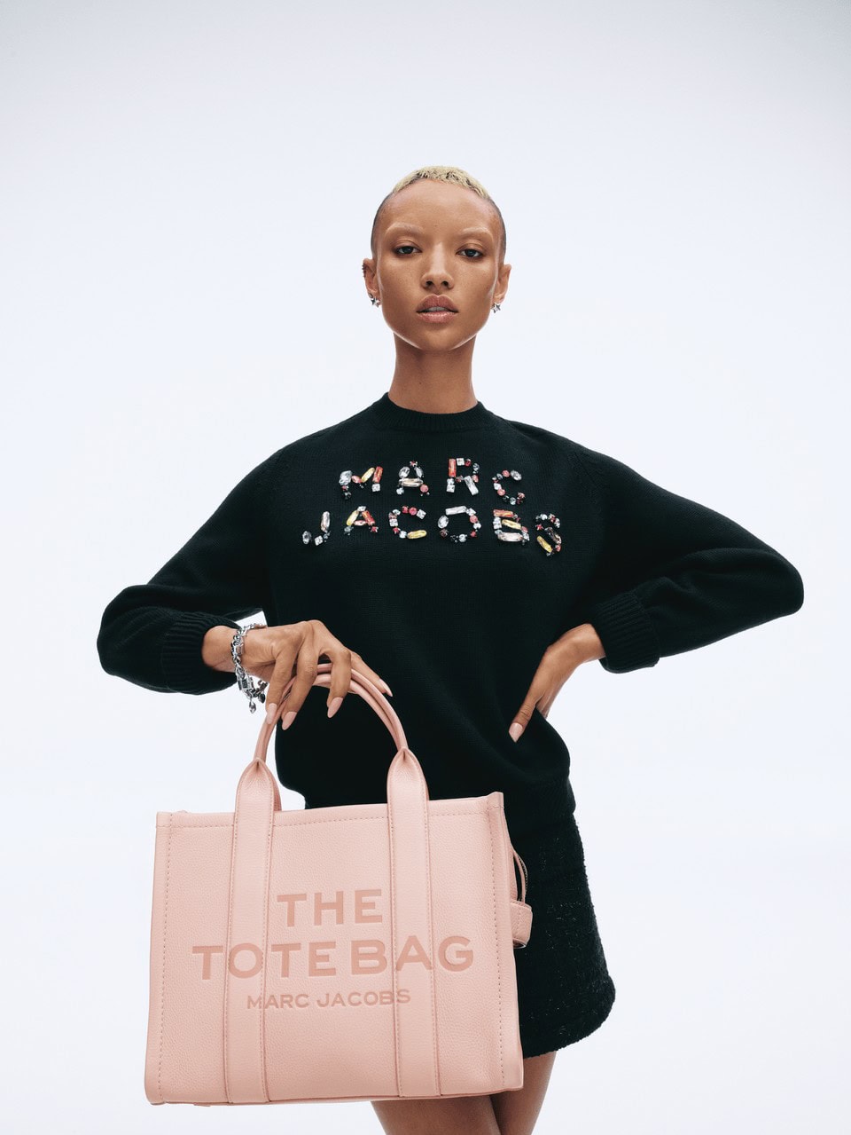 Model wearing black sweater holding a large pink tote bag against a plain white background