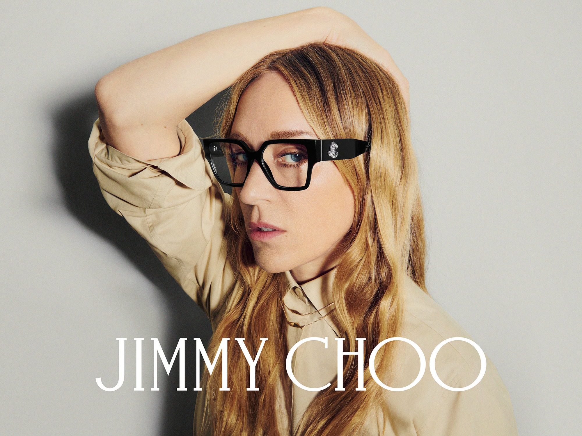 Chloë Sevigny wearing black eyeglasses and a beige shirt against a grey backdrop for Jimmy Choo