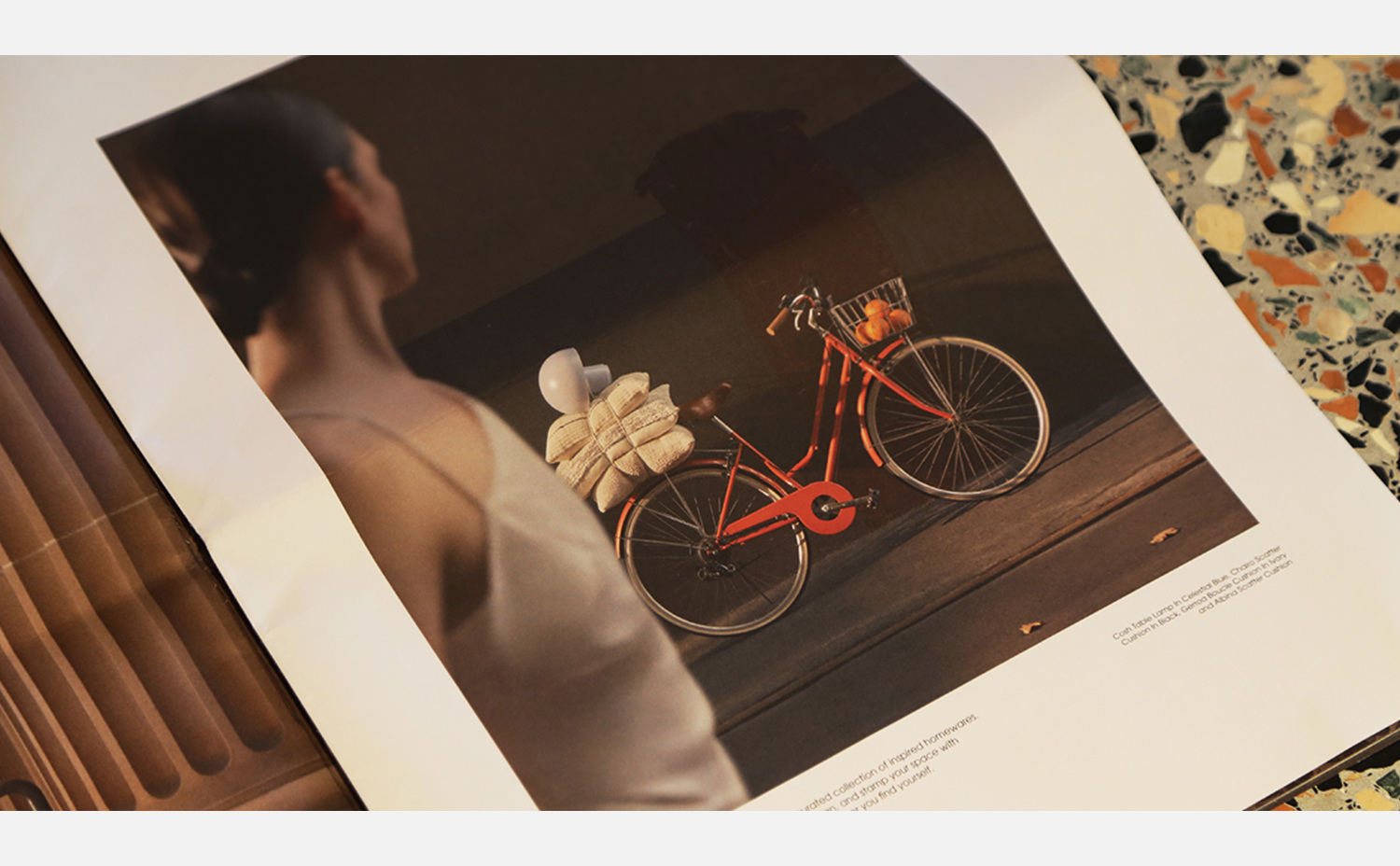 Red bicycle with a basket of oranges, and a picnic set, appearing in a warm-toned photograph displayed on a multicolored terrazzo table.