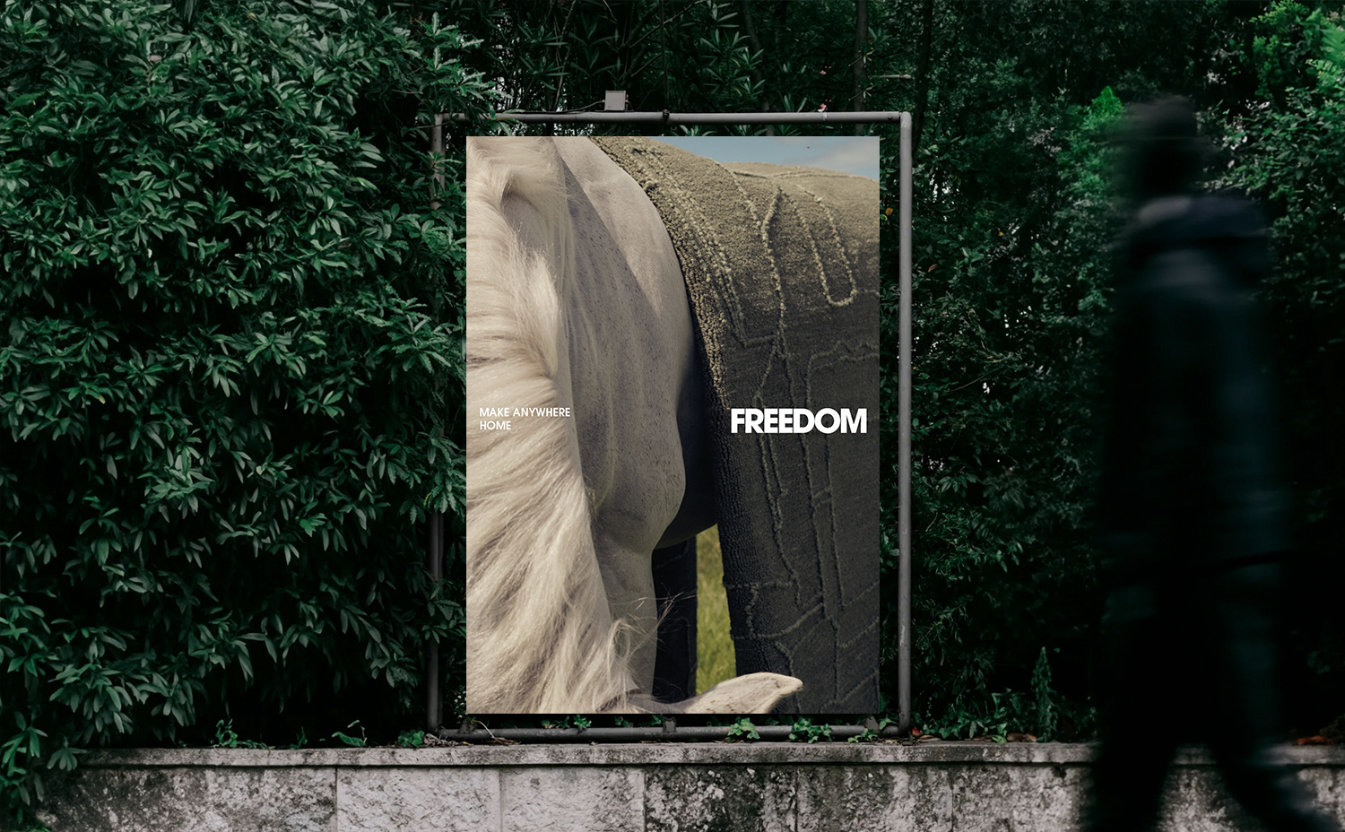Poster featuring sand and white hair, displayed outdoors with green bushes; silhouette of a person walks past the poster.
