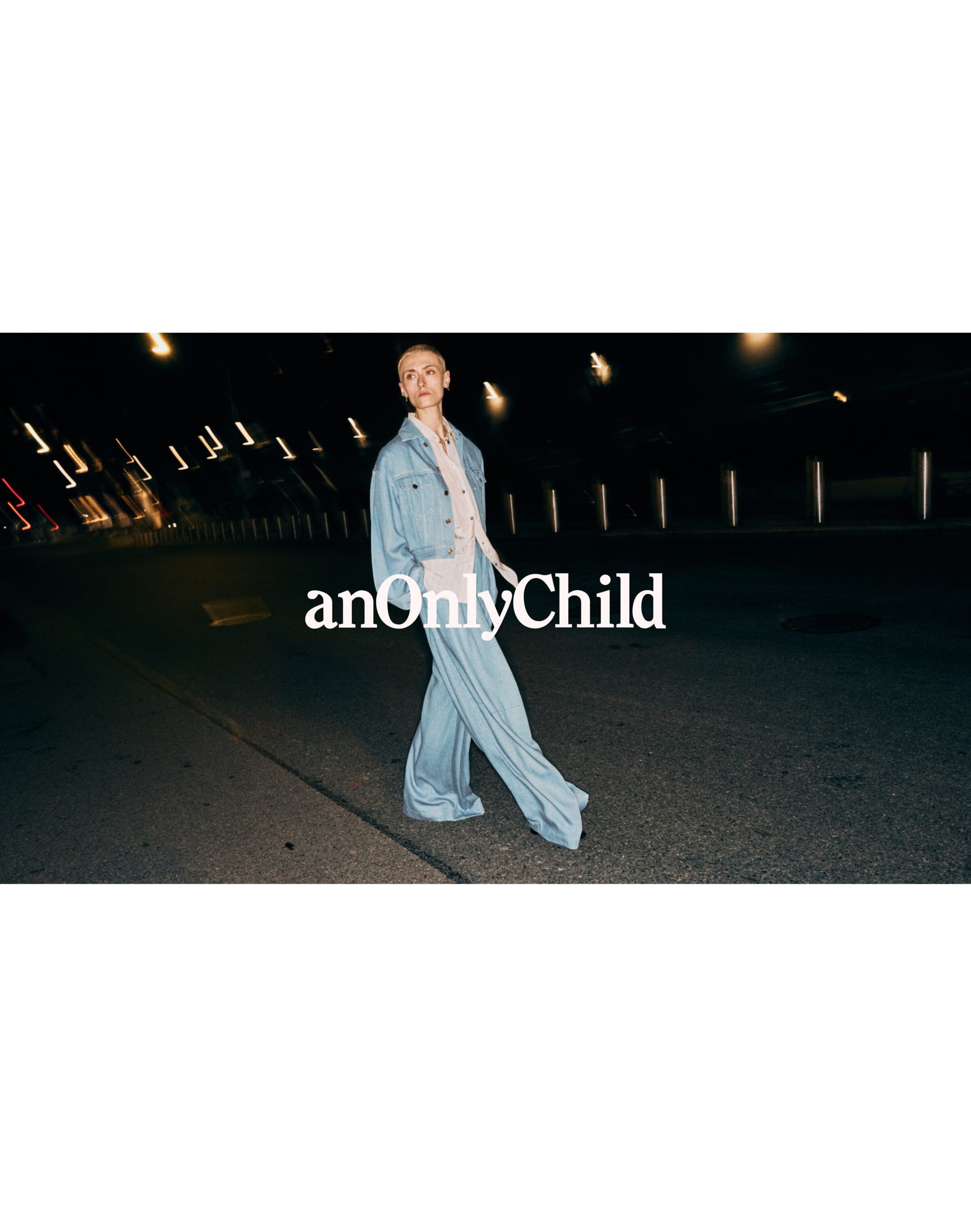 Model in light blue denim jacket and matching wide-leg trousers walking on a dark city street at night.