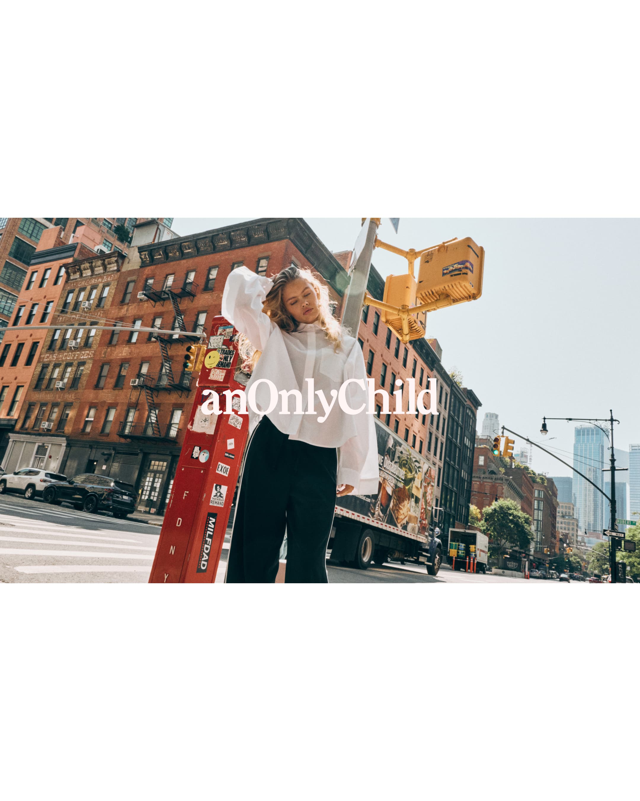 Model wearing a white blouse and dark trousers posing on a New York street next to a red box and traffic light