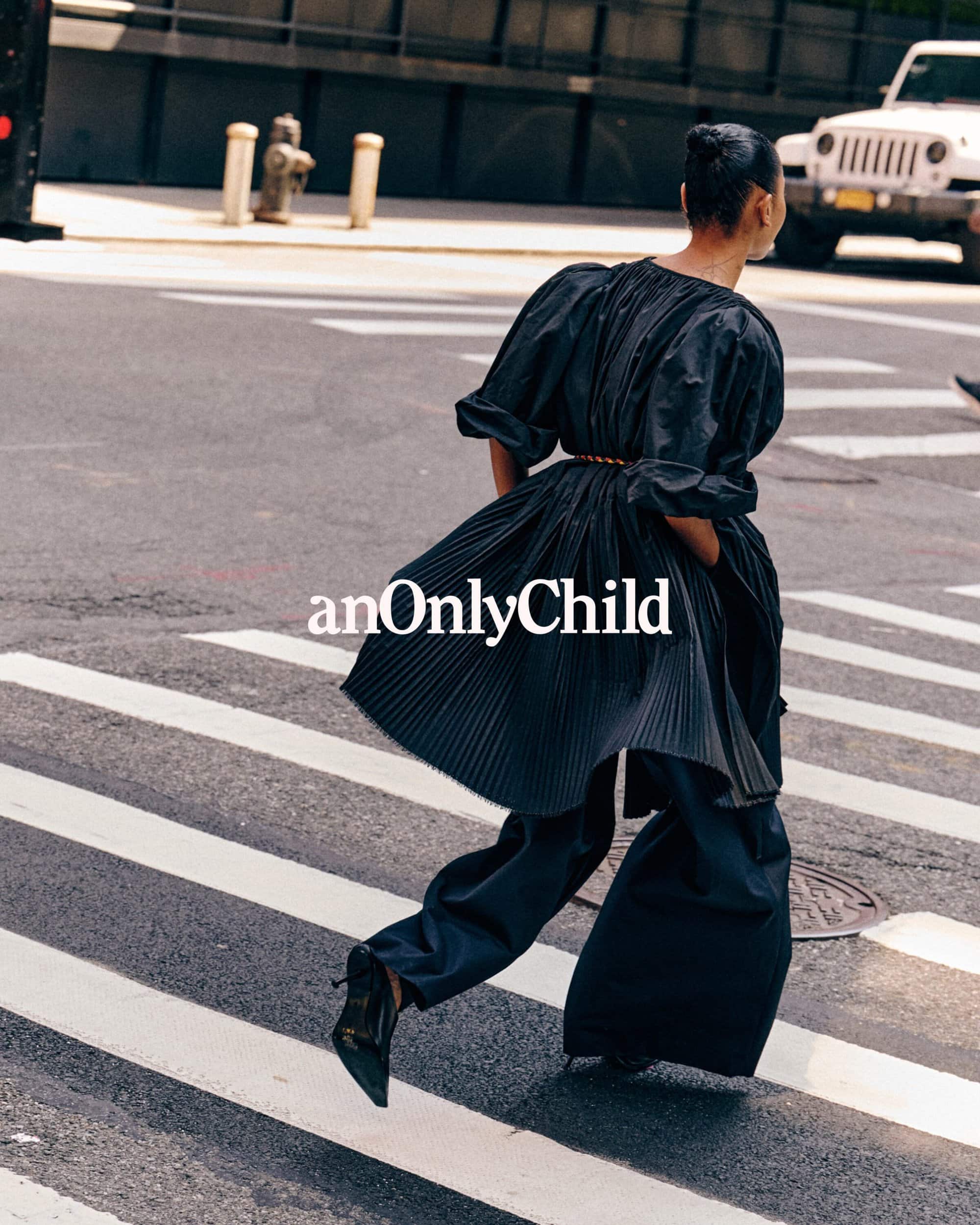 Model wearing a black pleated dress and wide trousers crossing a street for anOnlyChild