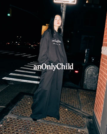 Model standing on a city street at night wearing a loose black sweatshirt and matching trousers for anOnlyChild