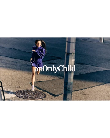 Model wearing a blue athletic tracksuit running across an asphalt street with a manhole cover near a utility pole.