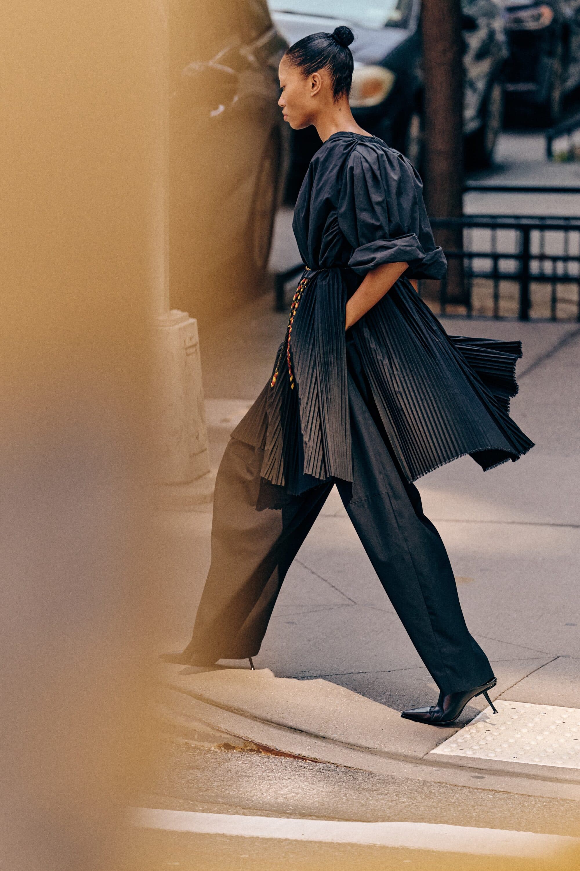 Black woman walking outdoors wearing a black pleated tunic top and wide-leg trousers for anOnlyChild Spring 2025 ad campaign.