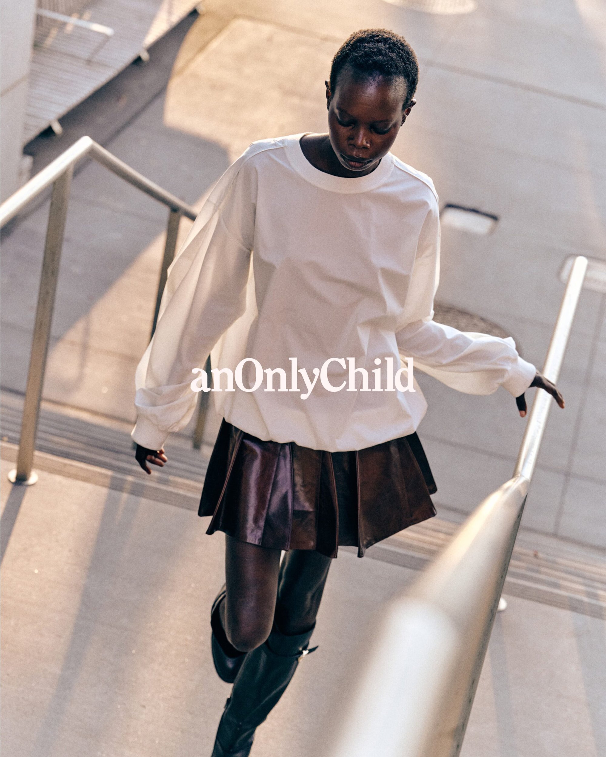 Model in white long-sleeve top and dark pleated skirt walking down concrete outdoor stairs