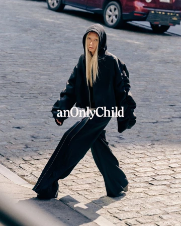 Model in black hoodie and wide trousers walking on a cobblestone street for anOnlyChild