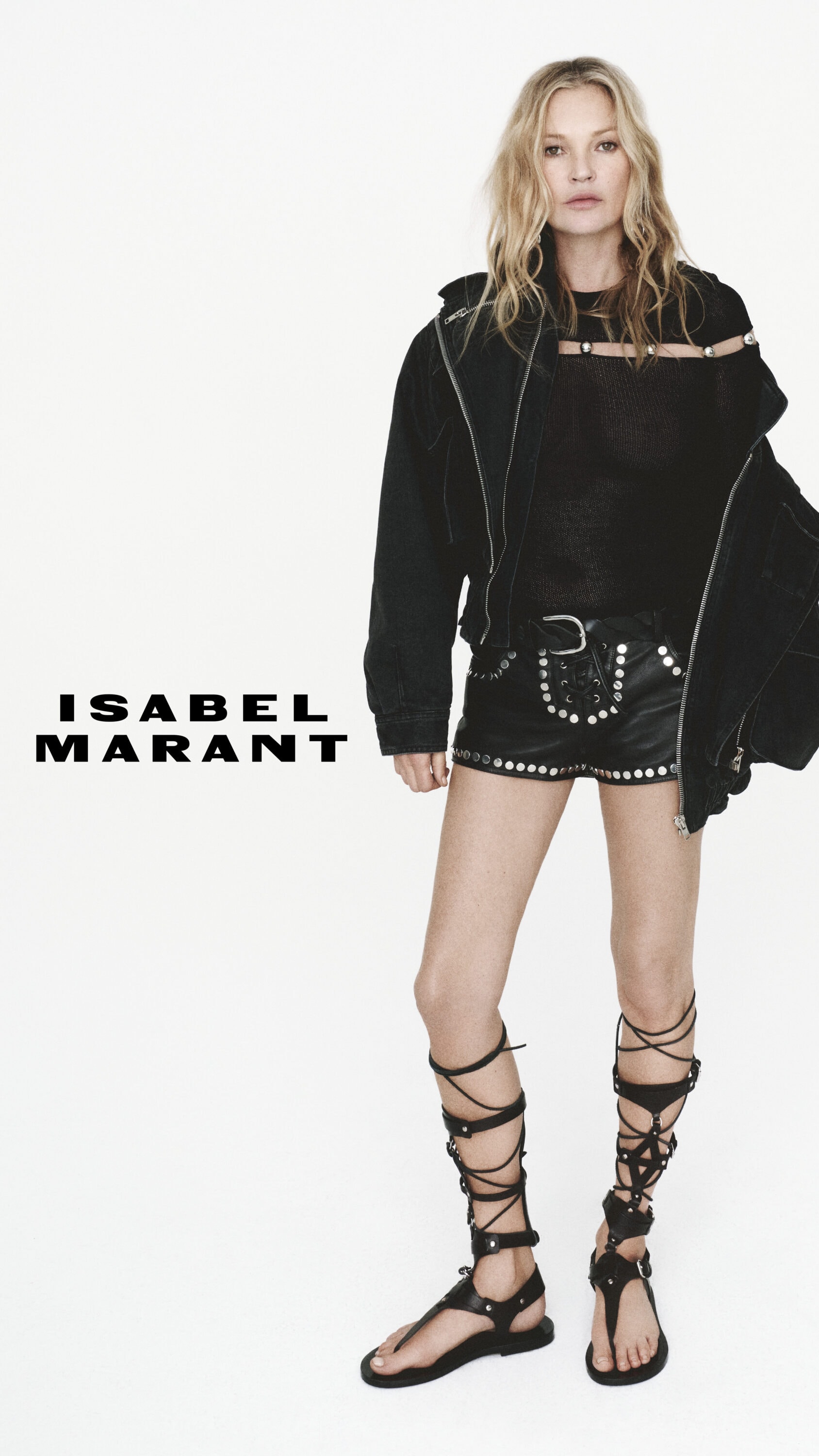 Kate Moss wearing black studded shorts, black jacket and gladiator sandals against a clean white background