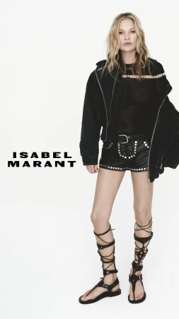 Kate Moss wearing black studded shorts, black jacket and gladiator sandals against a clean white background