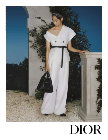 Model in a white Dior outfit with a black belt and handbag standing outdoors near stone architecture
