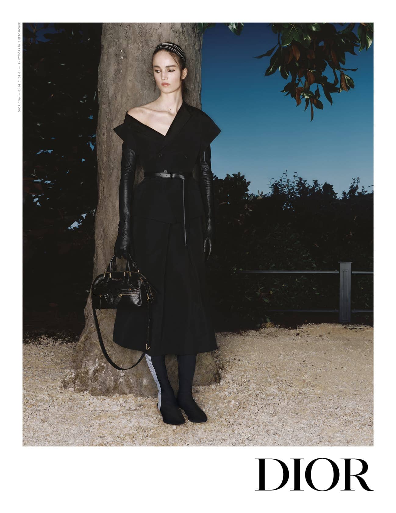 Model in black dress leaning against tree outdoors at dusk for Dior Spring 2025 ad campaign
