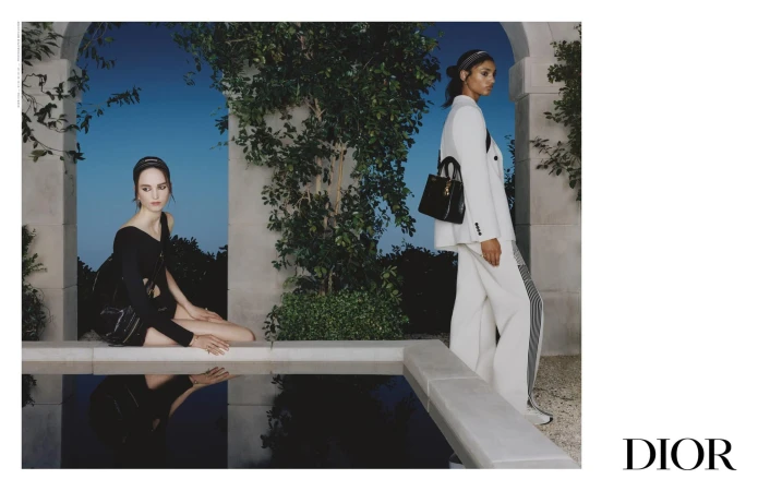 Two female models posing by an outdoor pool with archways and greenery for the Dior Spring 2025 ad campaign.