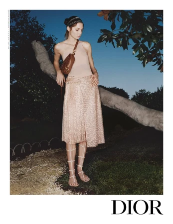 Model standing outdoors near a tree branch wearing a beige top, textured skirt, headband, and gladiator sandals.
