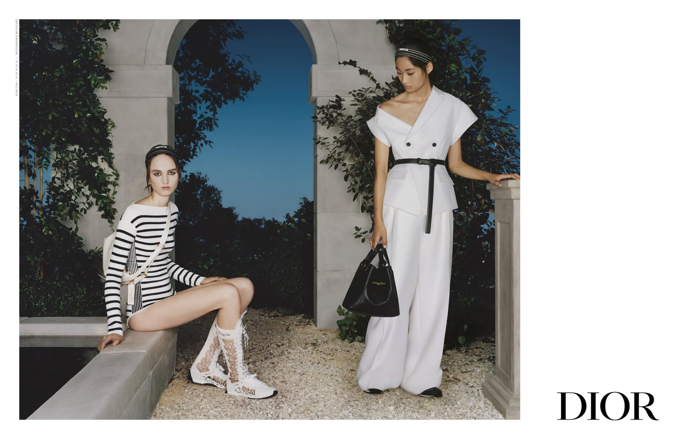 Two female models posing outdoors near architectural stonework for Dior Spring 2025 campaign, one seated and one standing.