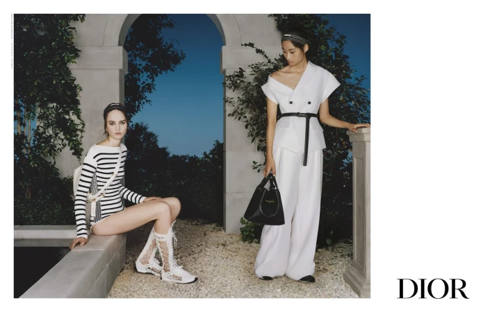 Two female models posing outdoors near architectural stonework for Dior Spring 2025 campaign, one seated and one standing.