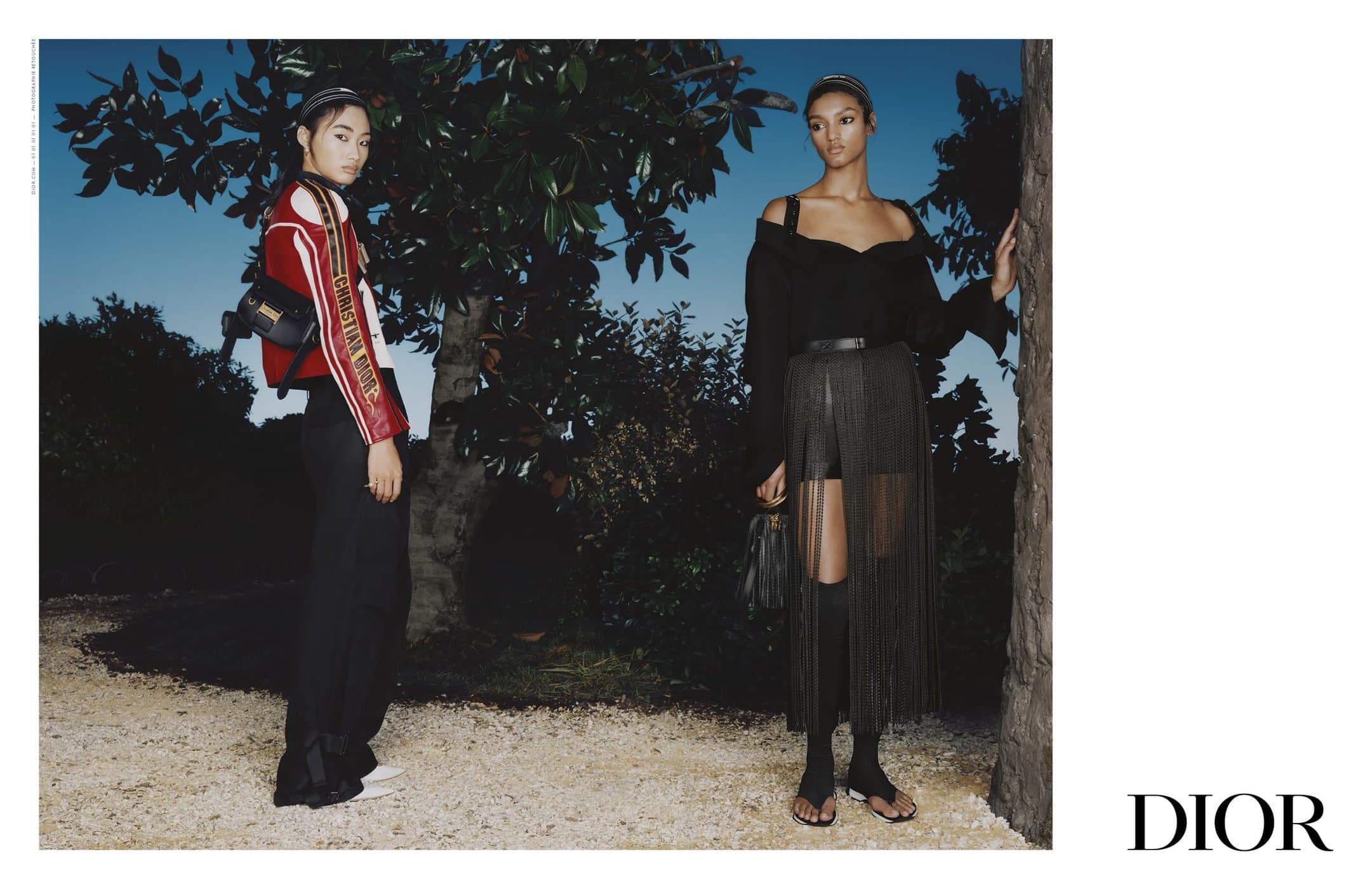 Two female models posing outdoors at dusk wearing Dior Spring 2025 campaign attire with trees and gravel pathway.