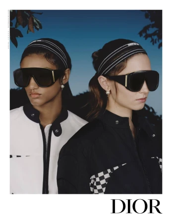Two female models wearing oversized black sunglasses and headbands against a blue sky background for Dior ad campaign.