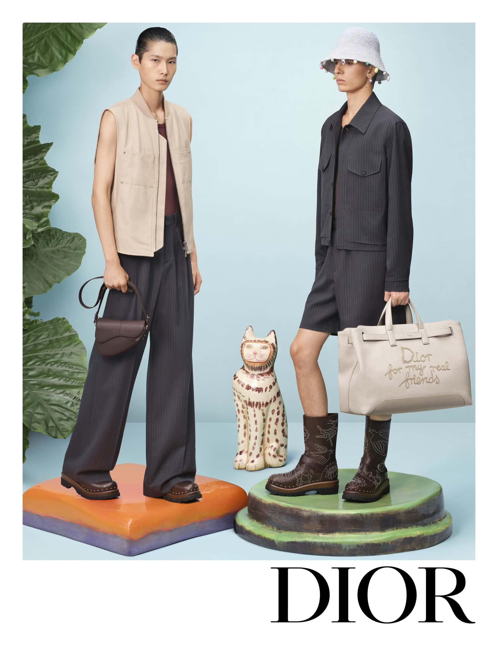 Two models posing on coloured pedestals with a ceramic cat sculpture against a pale blue background for Dior ad campaign
