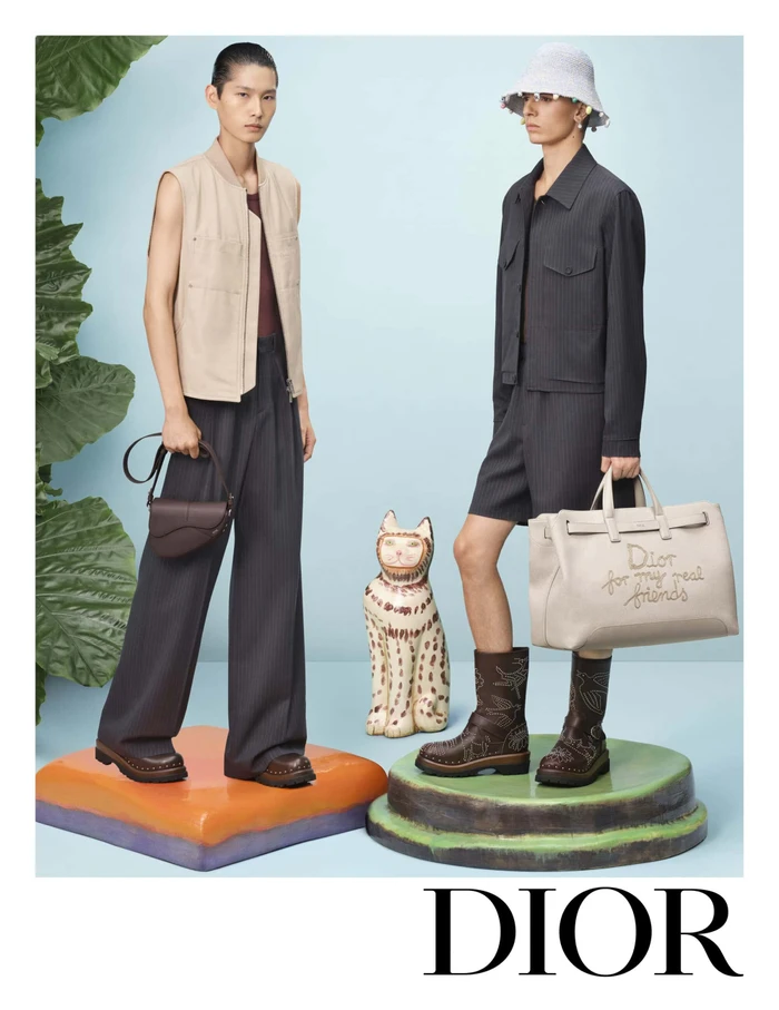 Two models posing on coloured pedestals with a ceramic cat sculpture against a pale blue background for Dior ad campaign