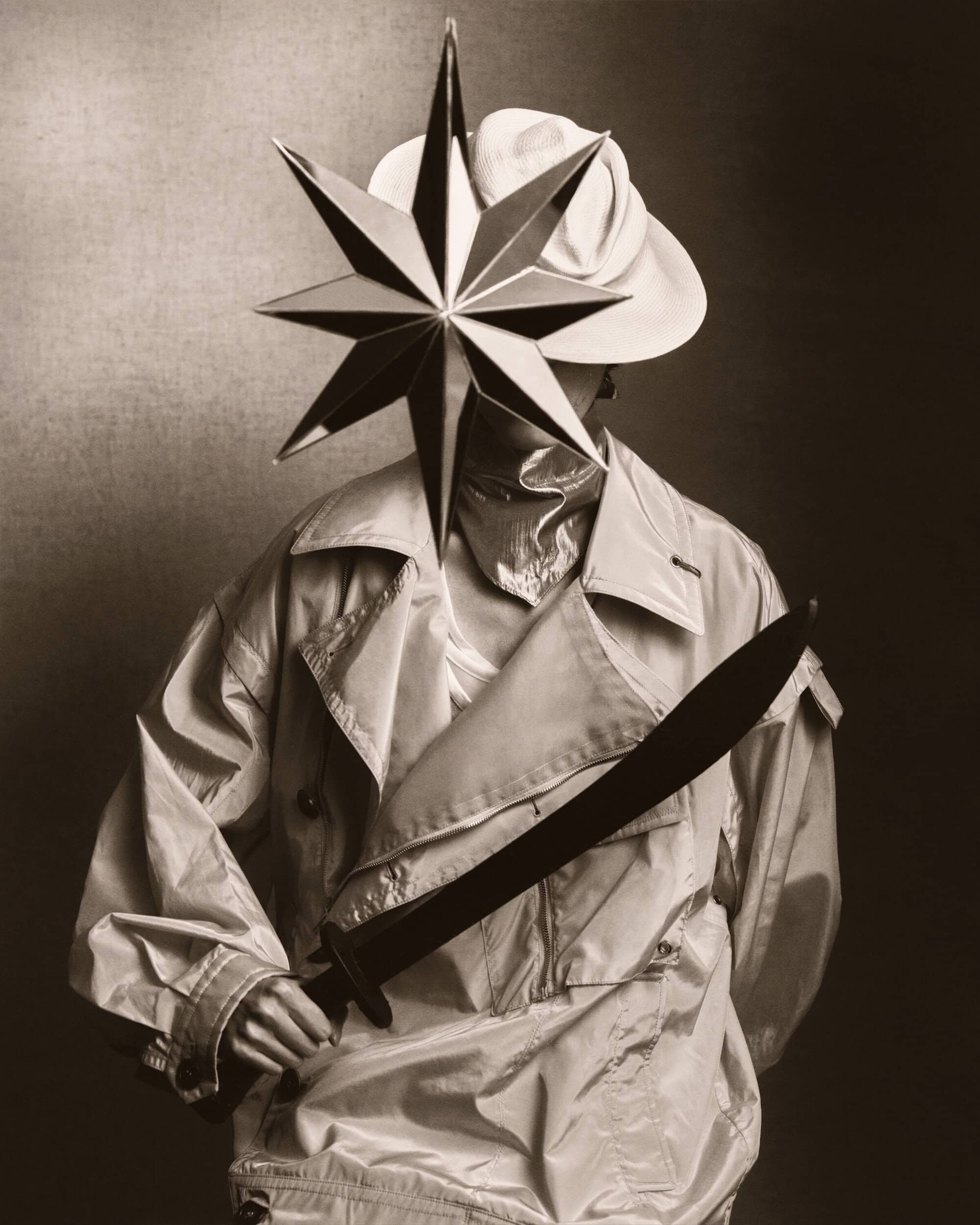 Monochrome portrait of a person wearing a hat and light jacket, holding a sword, with a large star obscuring their face.