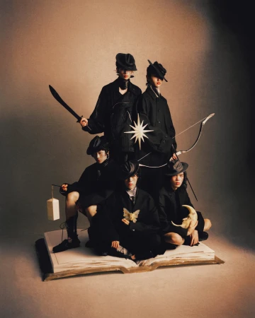 Five models dressed in black attire posing on a large open book prop holding props against a neutral studio backdrop