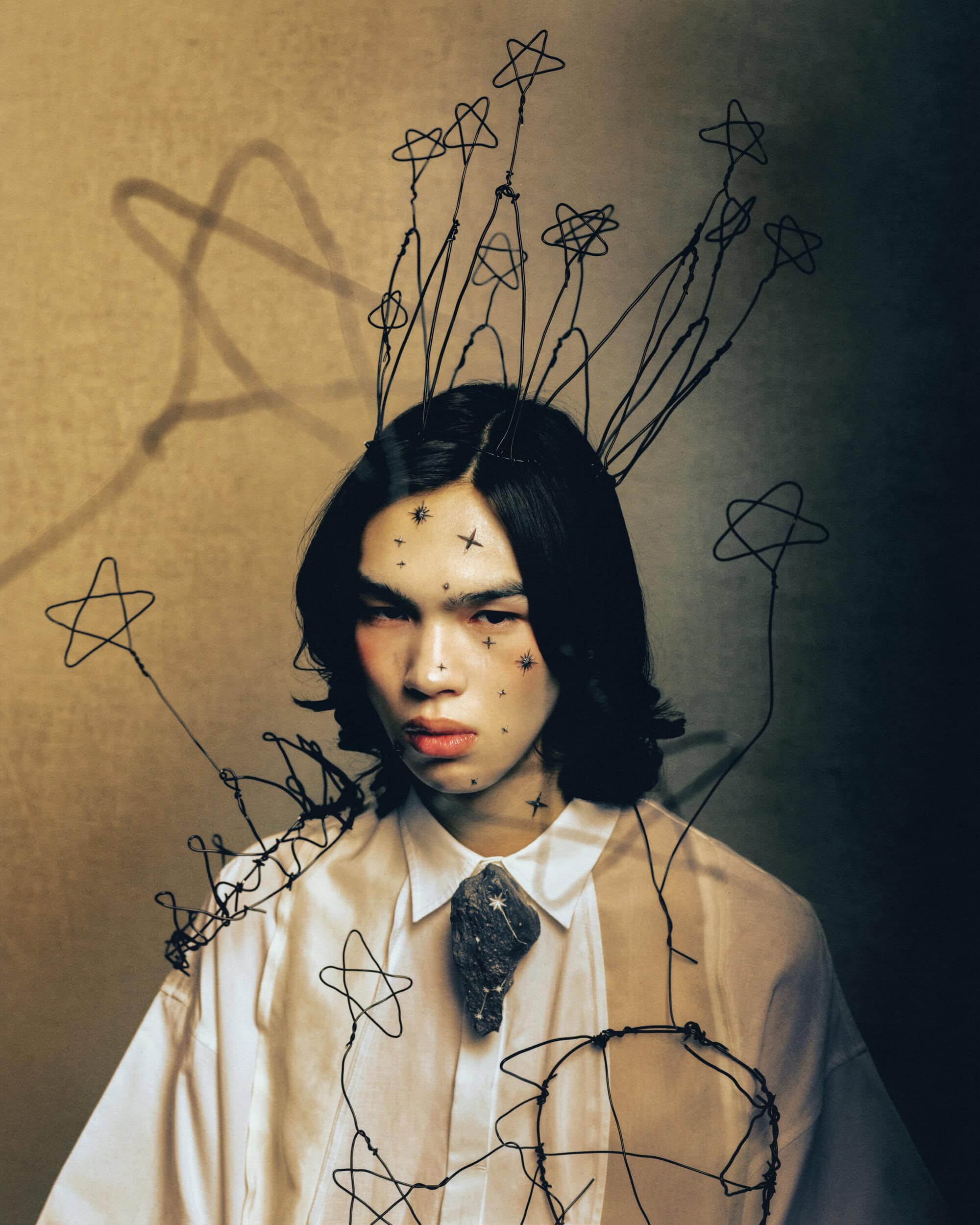 Portrait of a model wearing a white shirt with wire star sculptures floating around the head for the Songzio spring 2025 ad campaign