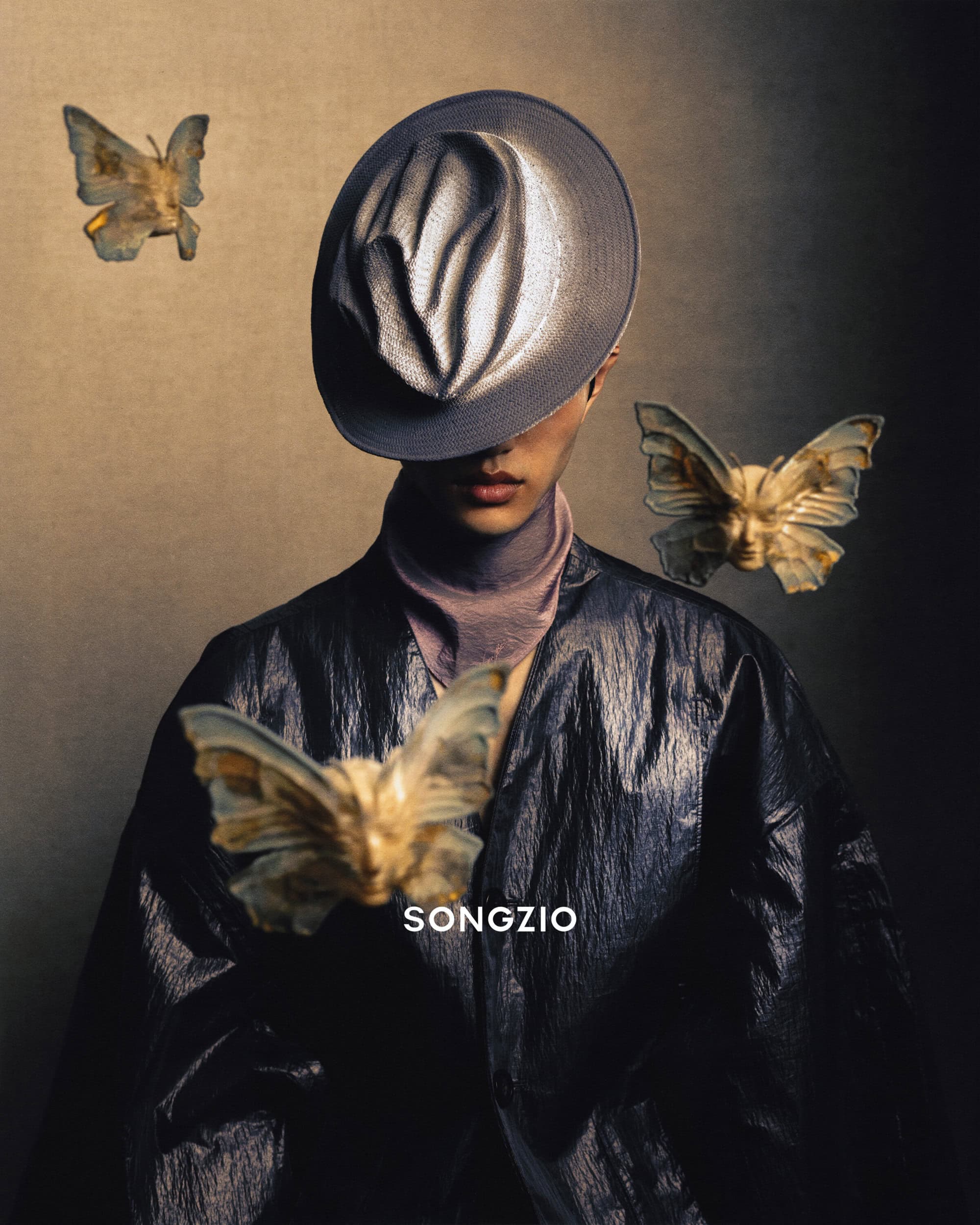 Model wearing a grey hat and dark jacket surrounded by floating butterfly sculptures with human faces for Songzio