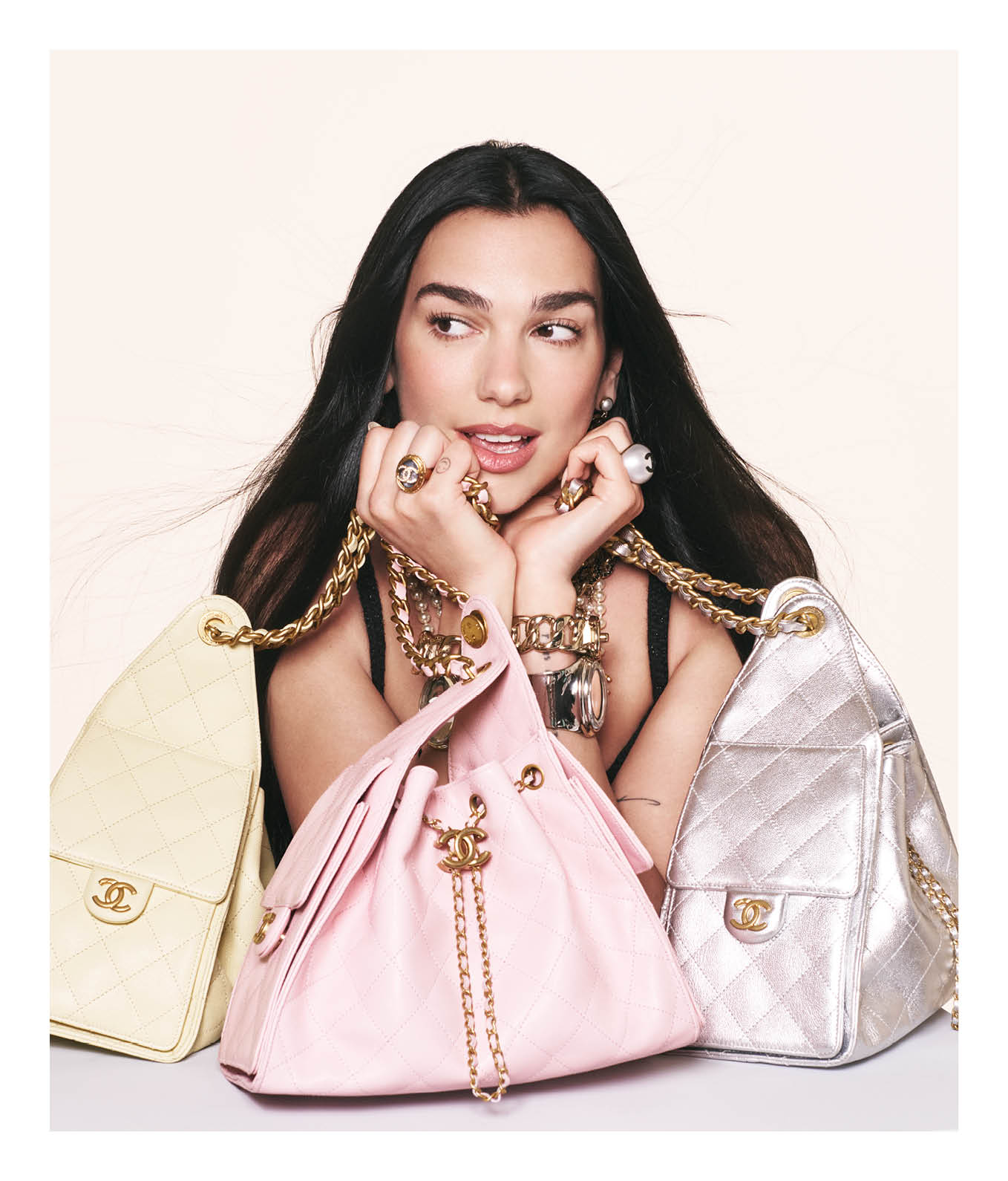 Dua Lipa holding multiple quilted Chanel handbags in an ad campaign by David Sims against a light background