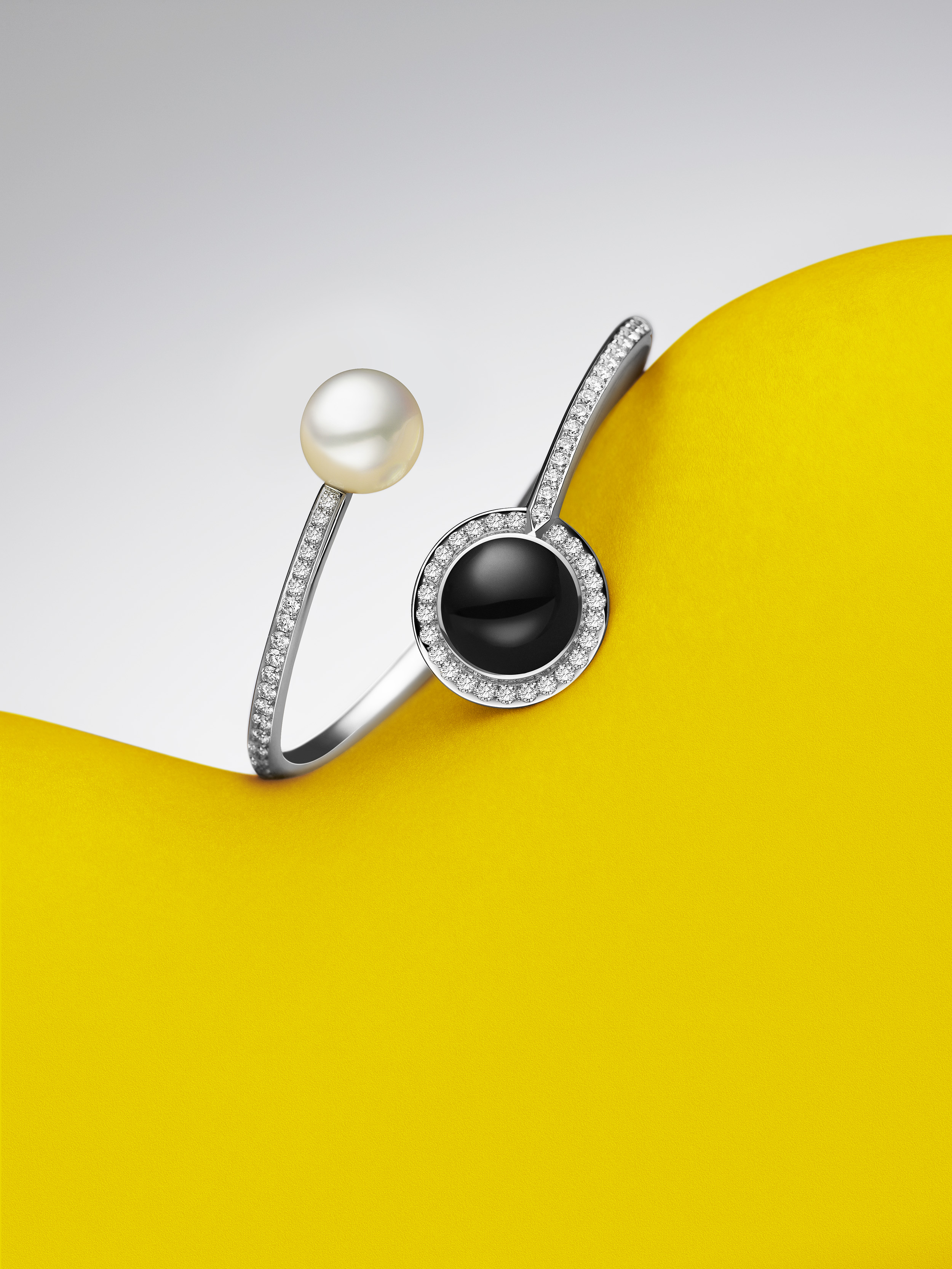 Elegant silver cuff bracelet featuring a pearl and black stone encircled by diamonds, showcased against a vibrant yellow backdrop.