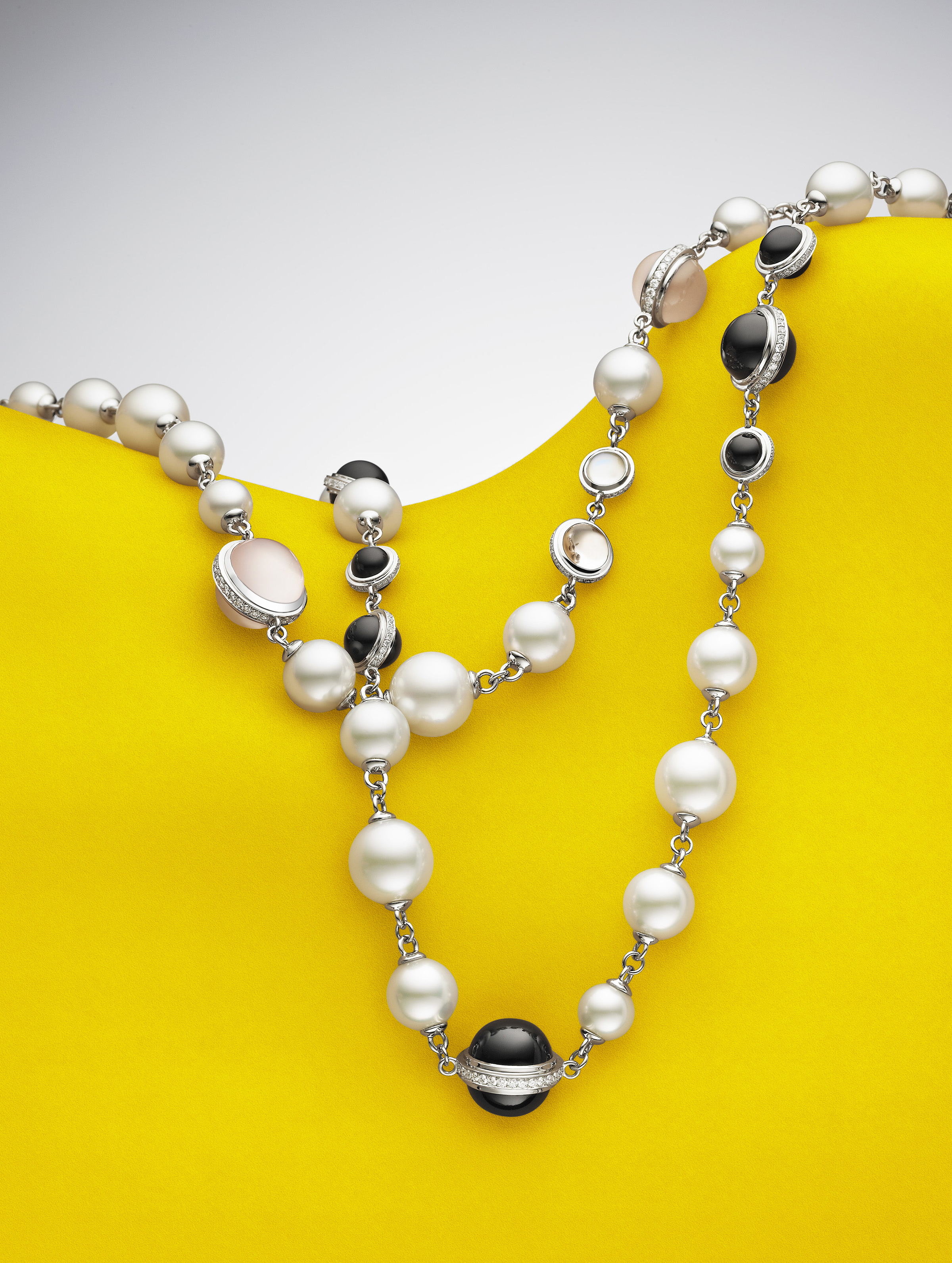 Elegant pearl necklace with black and pink stones on a vibrant yellow backdrop, showcasing fine jewelry and studio lighting.