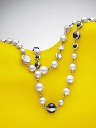 Elegant pearl necklace with black and pink stones on a vibrant yellow backdrop, showcasing fine jewelry and studio lighting.