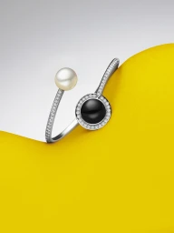 Paspaley pearl and black stone ring with pavé diamonds resting against a bright yellow and white curved background.