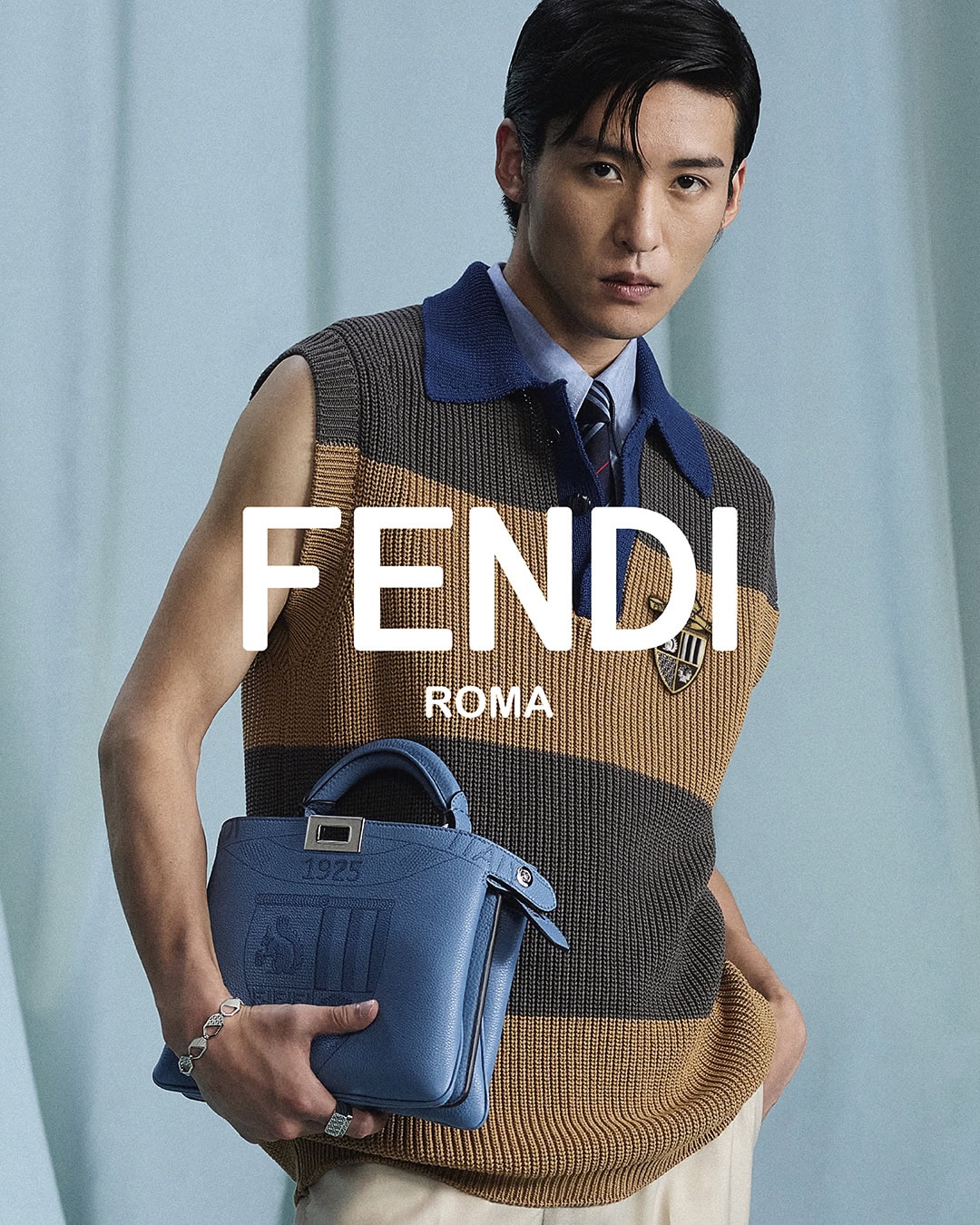 Ren Meguro wearing a striped knit vest holding a blue handbag for the Fendi Men's Spring 2025 campaign.