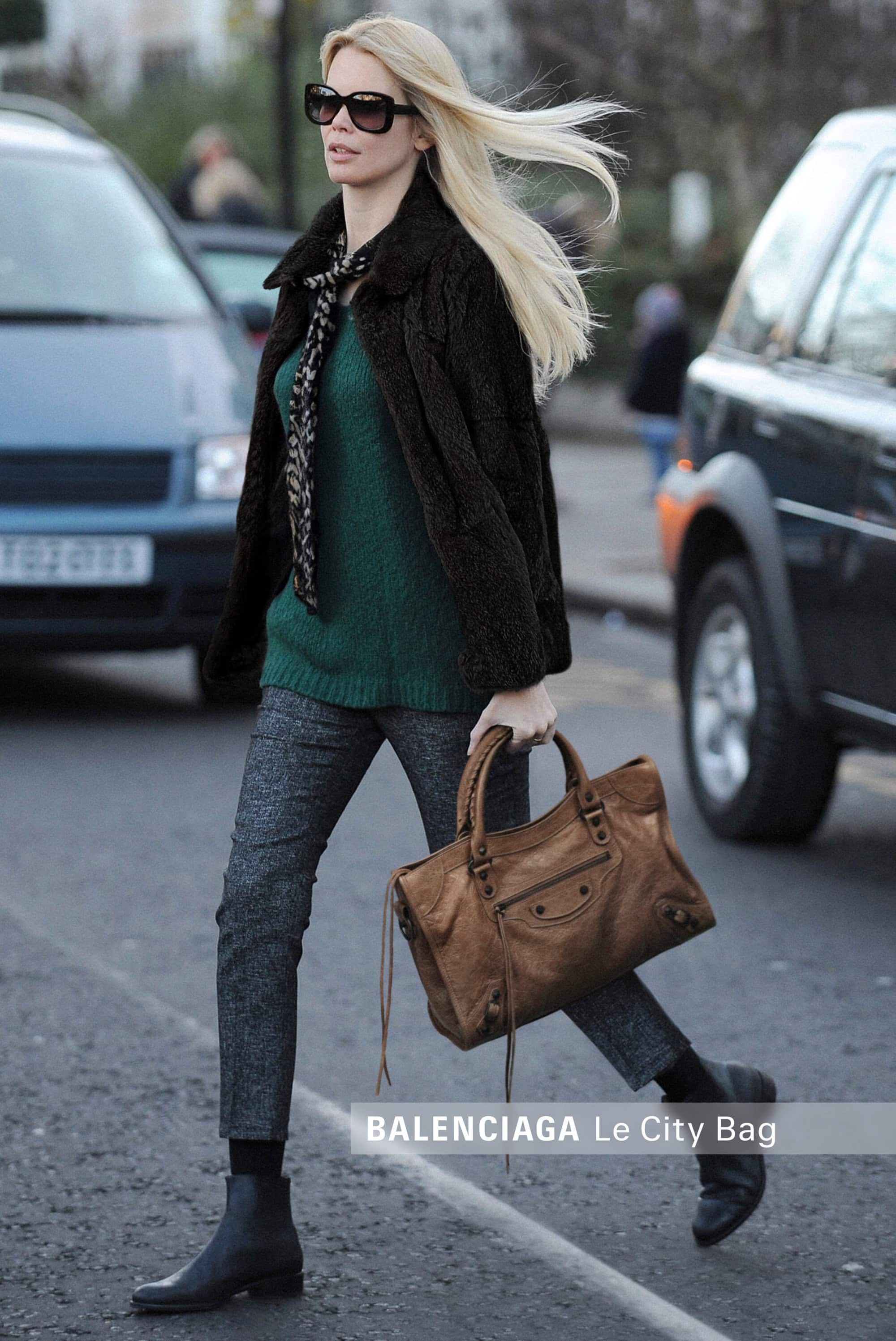 Claudia Schiffer walking down a city street holding a brown leather bag for the Balenciaga Le City campaign