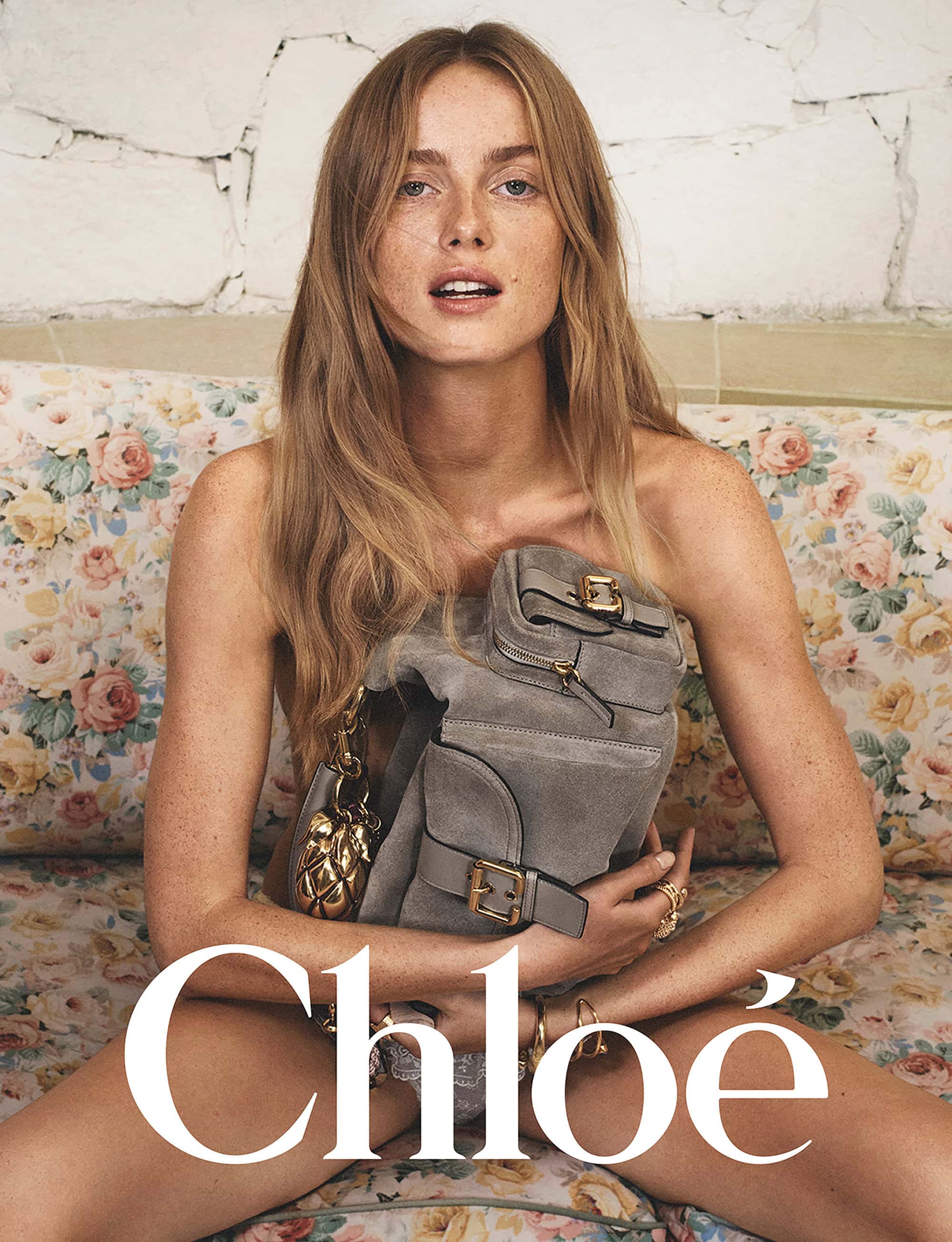 Model Rianne Van Rompaey holding a grey leather handbag against a floral patterned sofa for Chloé Spring 2025 campaign