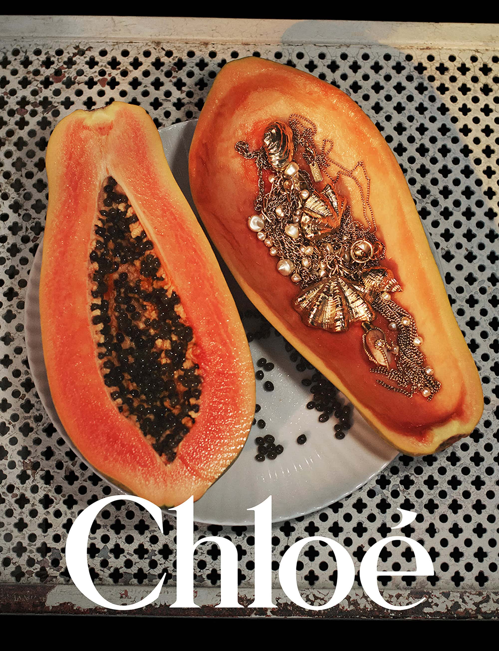 A halved papaya filled with gold jewellery resting on a plate atop a perforated metal surface