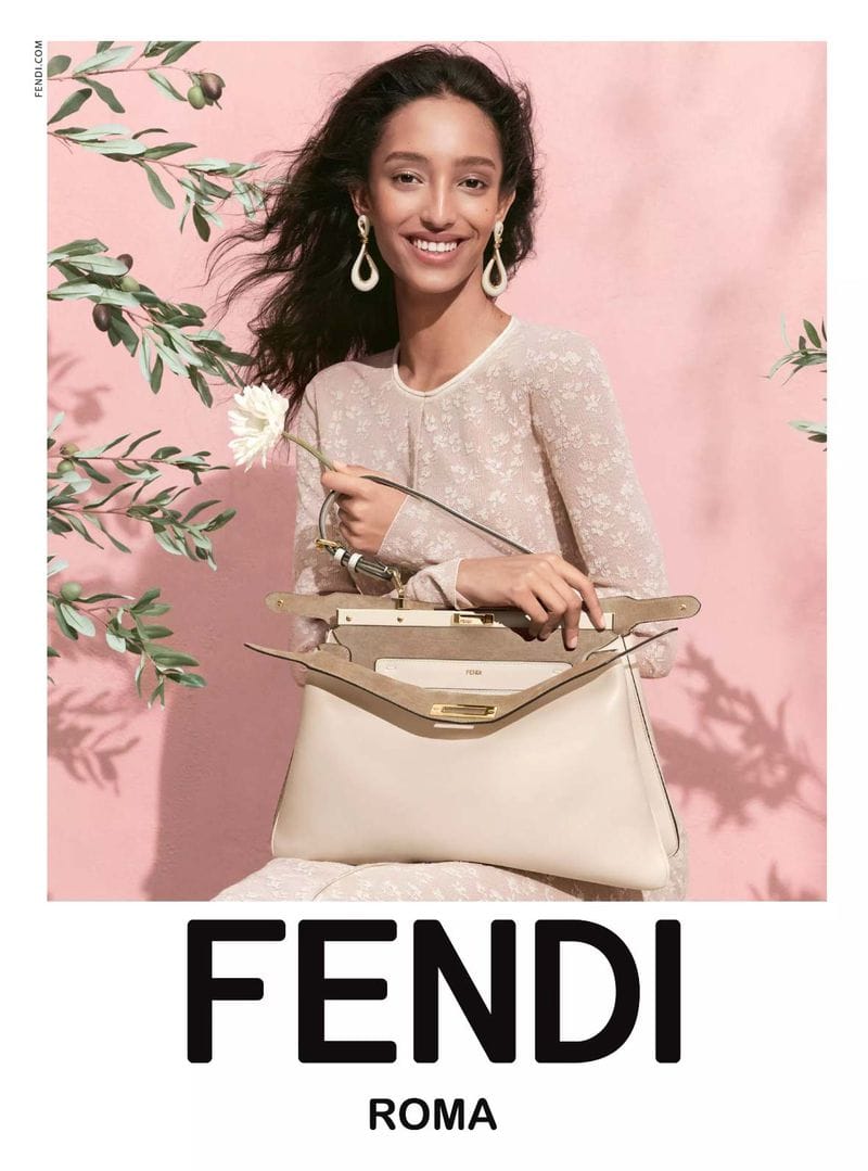 Model holding white handbag and flower against pink wall with olive branch shadows