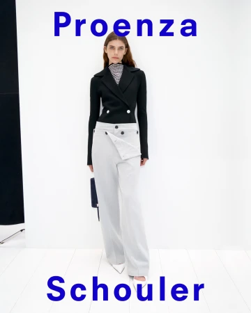 Model standing against a white backdrop wearing a black double-breasted jacket and light grey trousers
