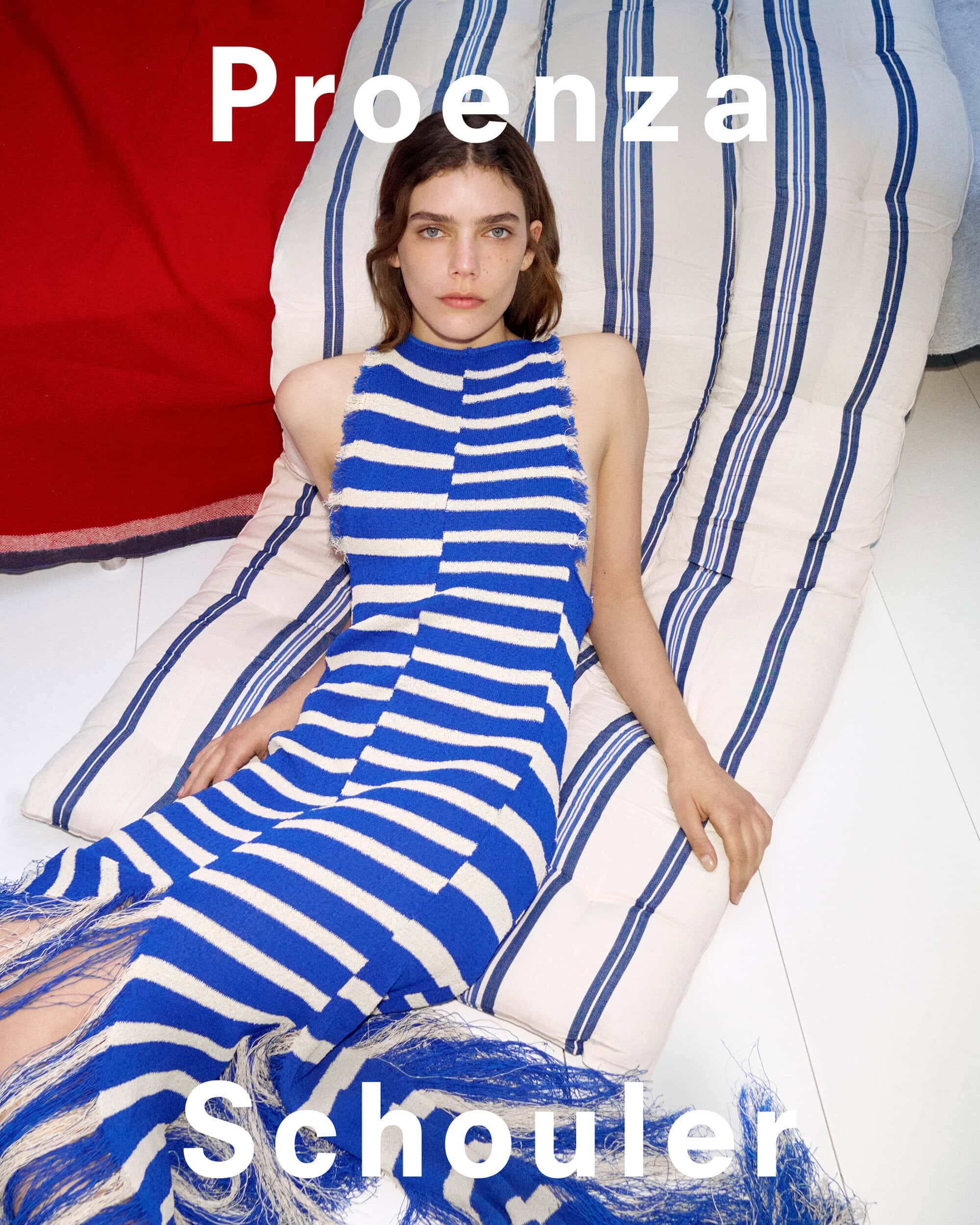 Model in a blue and white striped dress reclining on a striped cushion for Proenza Schouler