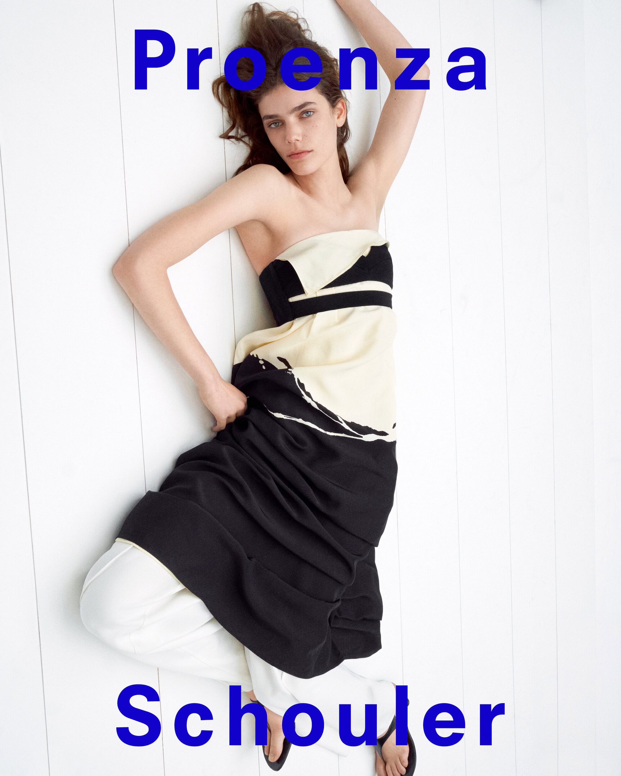 Model lying on white wooden floor wearing strapless black and ivory dress for Proenza Schouler