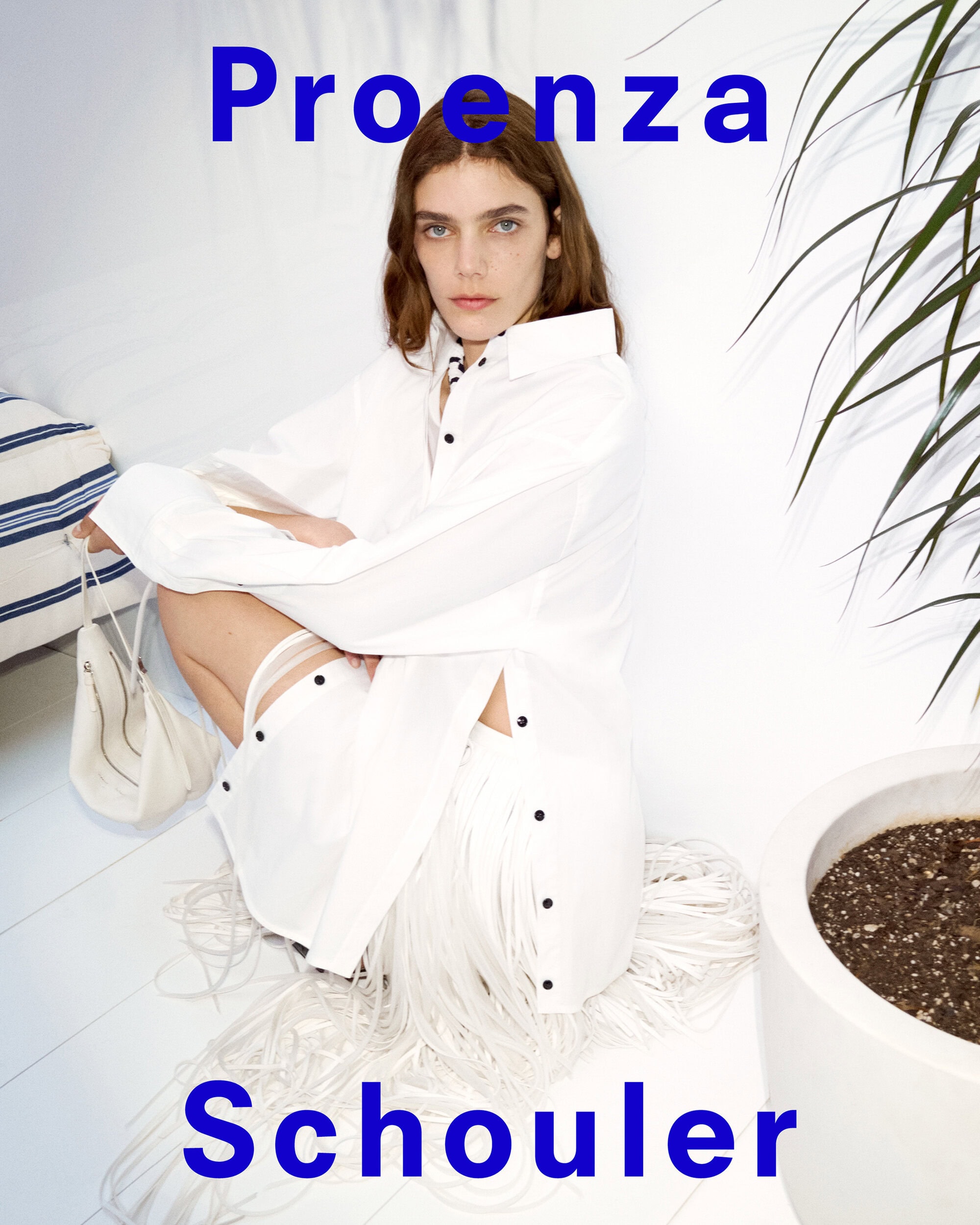 Model crouching wearing a white buttoned shirt and fringe skirt with a white bag for Proenza Schouler