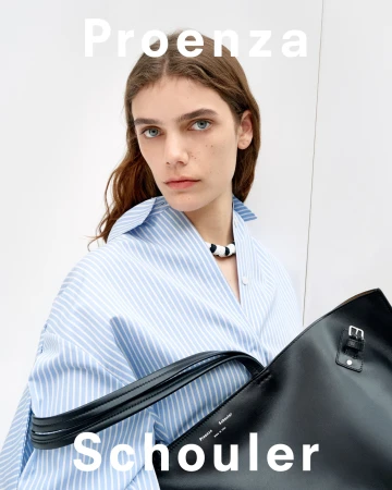 Model wearing a blue and white striped shirt holding a large black leather handbag against a plain background