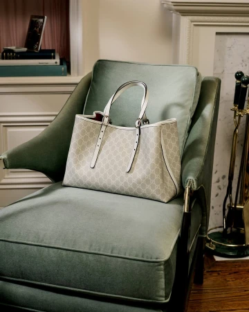 Gucci monogram tote bag resting on a pale green velvet armchair inside a domestic living room setting