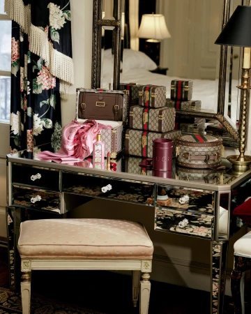 Gucci monogram vanity cases and pink silk scarf arranged on a mirrored dressing table in a bedroom