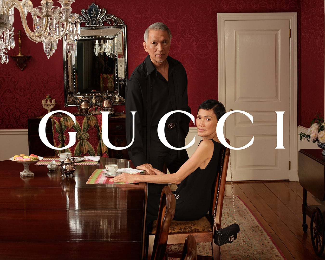 Man standing and woman seated at a dining table in a rich red interior for Gucci Valentine's Day campaign
