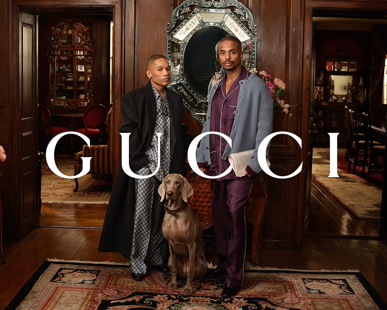 Two men standing indoors with a dog on an ornate rug inside a wood-paneled room for Gucci advertising campaign